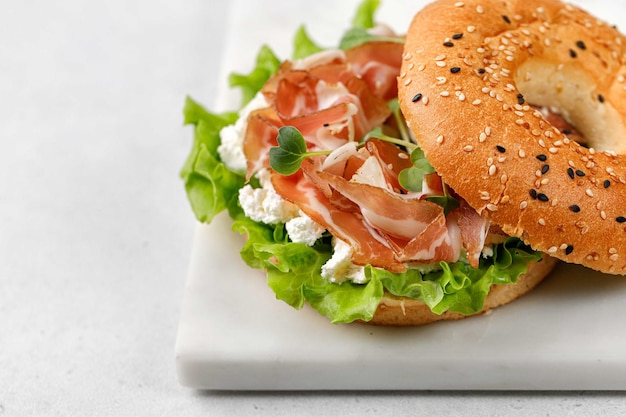 Sandwich met ricotta prosciutto en microgreens bagel met ham voor ontbijt op marmeren bord