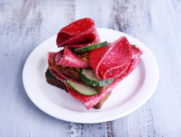 Sandwich met salami en komkommer op plaat op een houten tafel achtergrond kleur