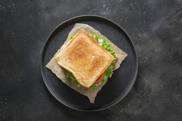 Sandwich met spek, tomaat, ui, salade op zwarte achtergrond. Geïsoleerd. Uitzicht van boven.