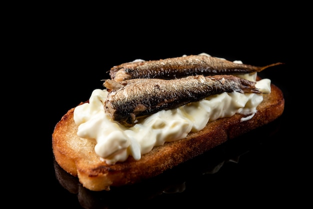 Sandwich met sprot, eieren en mayonaise op zwarte ondergrond.