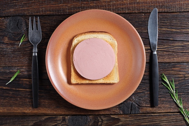 Sandwich met worst en geroosterd brood op oude houten tafel, bovenaanzicht