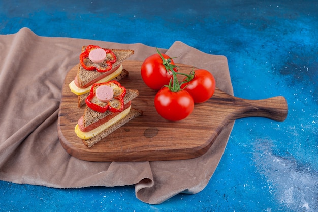 Sandwich met worst en hele tomaten op een snijplank op stukjes stof, op de blauwe tafel.