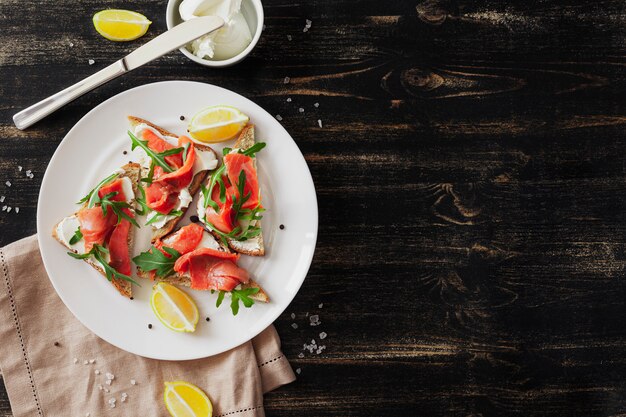 Sandwich met zalm, kaas, rucola en citroen op een witte plaat op een zwarte tafel