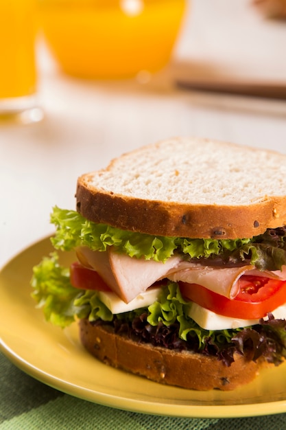 Sandwich op een witte plaat met kalkoenfilet, tomaat, sla en kaas op tafel