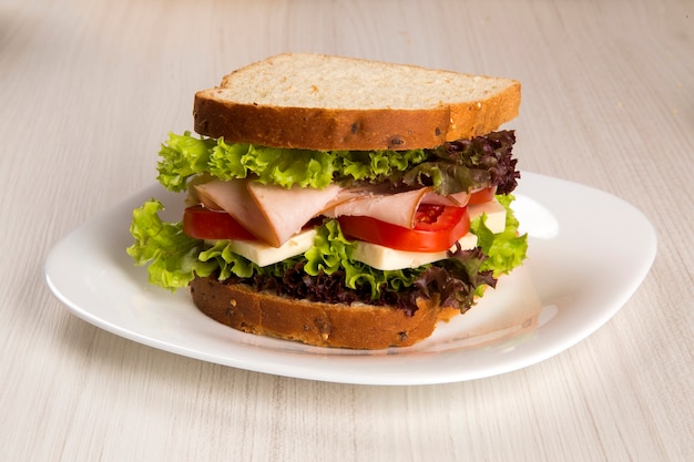 Sandwich op een witte plaat met kalkoenfilet, tomaat, sla en kaas op tafel