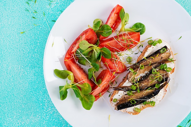 Sandwich - smorrebrod with sprats and tomatoes salad on white plate