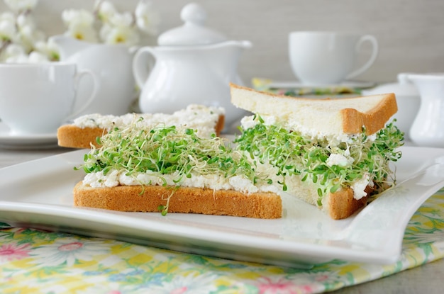 Un panino germogliato di germogli di erba medica con morbida ricotta e una tazza di caffè o tè