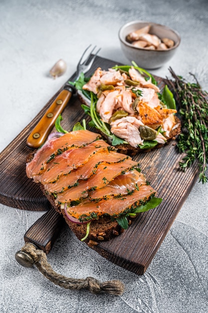 Sandwich toast met warme en koude gerookte zalm, rucola en roomkaas op een houten bord