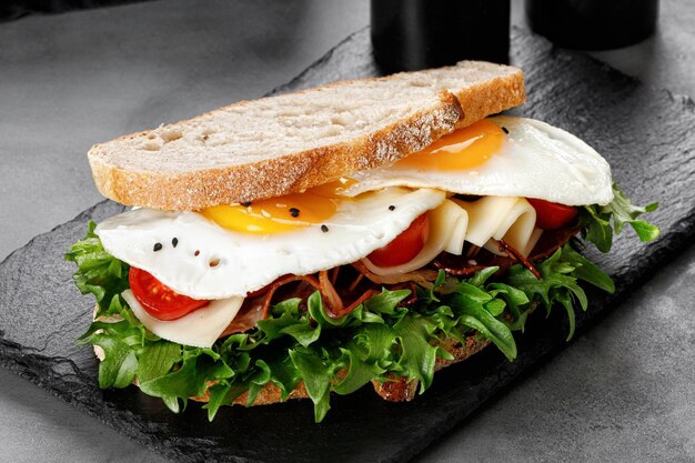 Sandwich toast with eggs bacon cheese green lettuce on black slate board Fresh and healthy breakfast