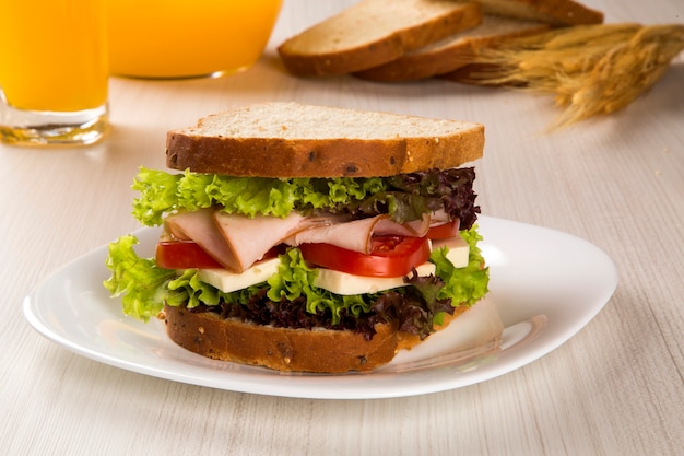 Сэндвич на белой тарелке с грудкой индейки, помидорами, листьями салата и сыром на столе