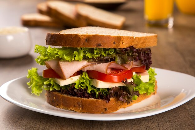 Sandwich on a white plate with turkey breast, tomato, lettuce and cheese on the table