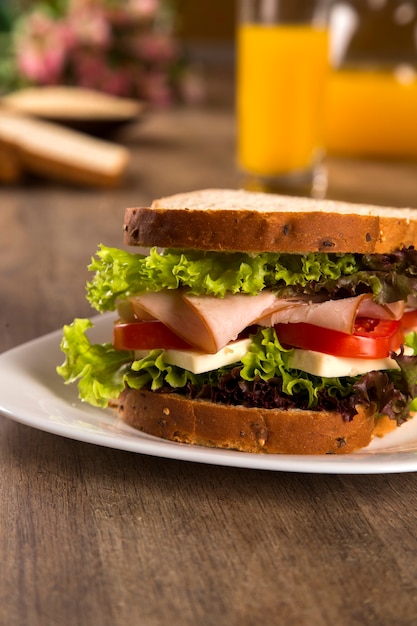 Sandwich on a white plate with turkey breast, tomato, lettuce and cheese on the table