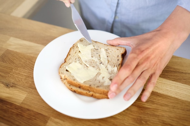 木製のキッチンテーブルの上にある白い皿のサンドイッチ女性がバターでパンを焼き朝食を調理しています