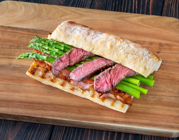 Sandwich with asparagus and slices of beef steak on the wooden board