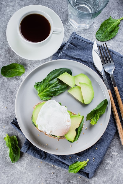 Panino con avocado, spinaci e uovo in camicia su pane integrale sul piatto sul retro di pietra