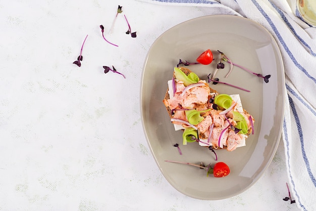 Sandwich with baked salmon, feta cheese, avocado and microgreens