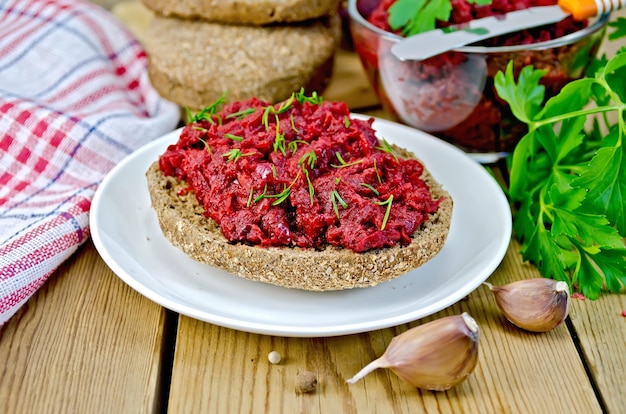 Sandwich with beet caviar and dill on a plate, garlic, parsley, a napkin on the background of wooden boards