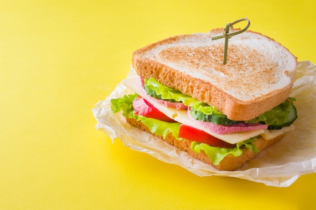 Бутерброд с сыром, ветчиной и свежими овощами на ярком желтом