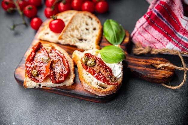 A sandwich with cheese, tomatoes, and olives on a wooden board