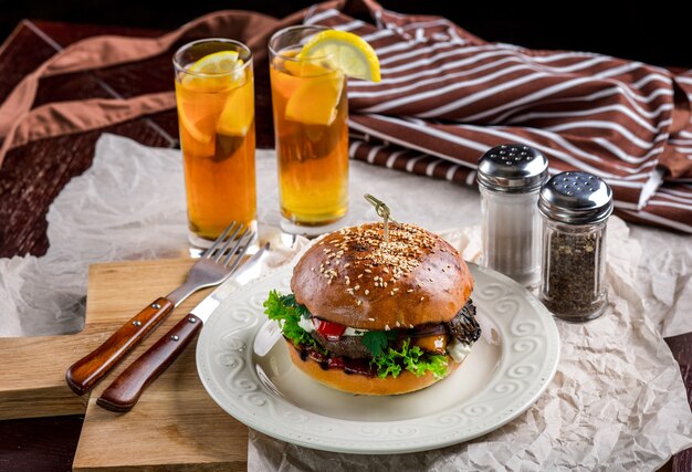 Sandwich with chicken burger, tomatoes, cheese and lettuce. Burger is on the table with paper and salt and pepper shakers. As well as two cocktails log Island Iced