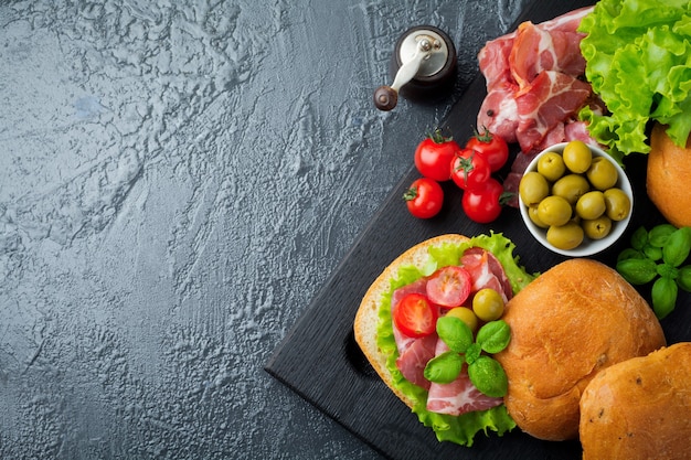 Sandwich with dried meat, jamon with cherry tomatoes, basil, ciabatta, olives on a black 