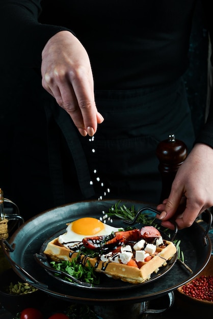 Sandwich with egg cheese salted fish and arugula on a plate in the hands of a chef on a rustic wooden background Belgian waffles On a black background