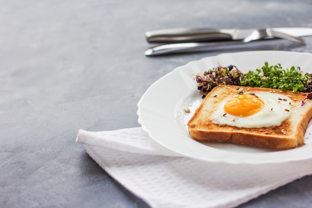 A sandwich with egg in the hole of the bread, microgreens, healthy food Breakfast, grey background