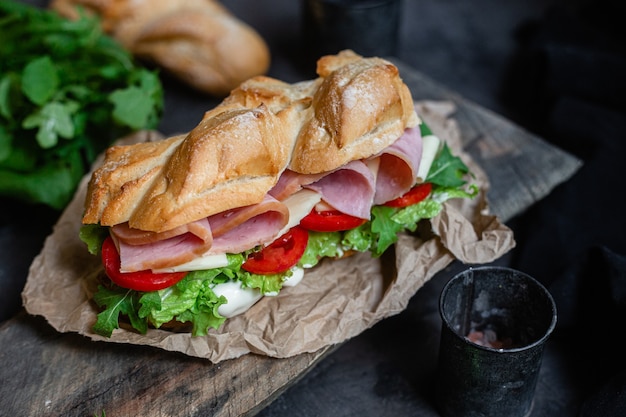 Foto panino con prosciutto formaggio pomodoro e lattuga su fondo scuro