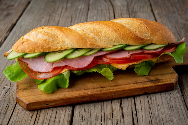 Sandwich with ham, cheese, tomatoes, cucumbers, lettuce on dark wooden background