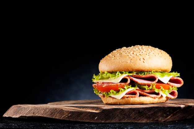 Sandwich with ham cheese and vegetables on a wooden board