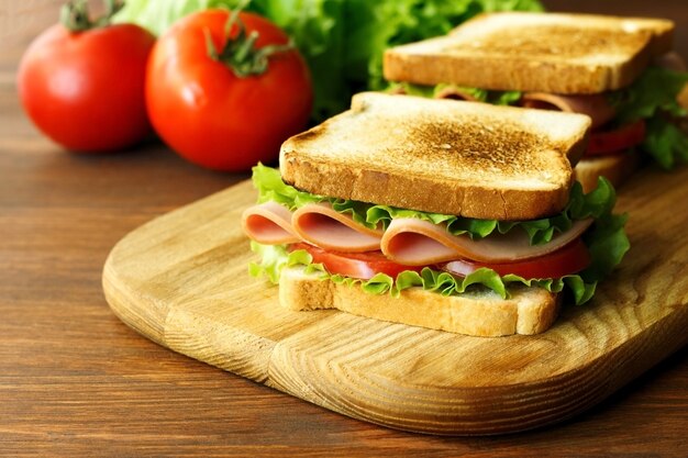 Sandwich with ham green lettuce and tomato on a wooden brown kitchen board