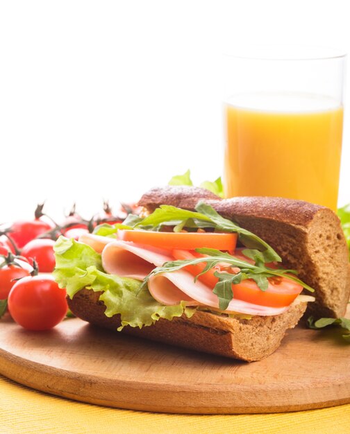 Sandwich with ham, tomato, lattuce and arugula with glass of orange juice with copy space.