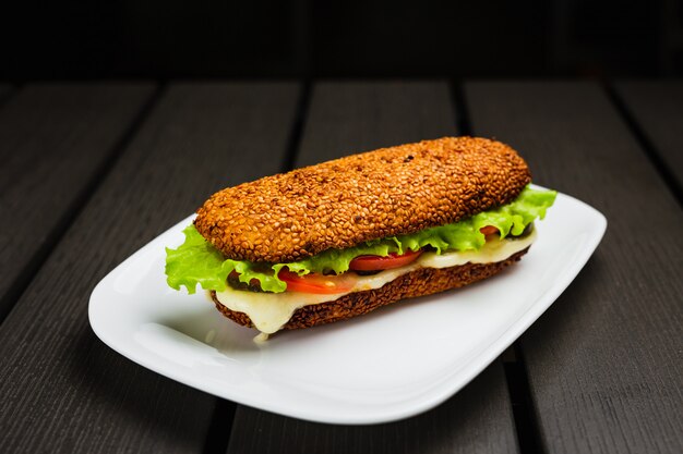 A sandwich with hot mozzarella, tomato, lettuce and pickles on a sesame bun