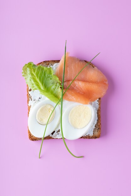 Фото Бутерброд с сыром маскарпоне, яйца, лосось на розовой стене. вид сверху.