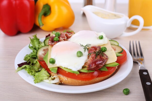 Sandwich with poached eggs bacon and vegetables on plate on wooden background
