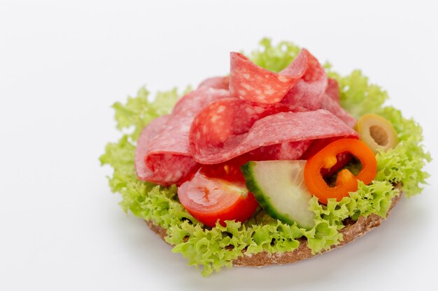 Sandwich with salami sausage on white surface.