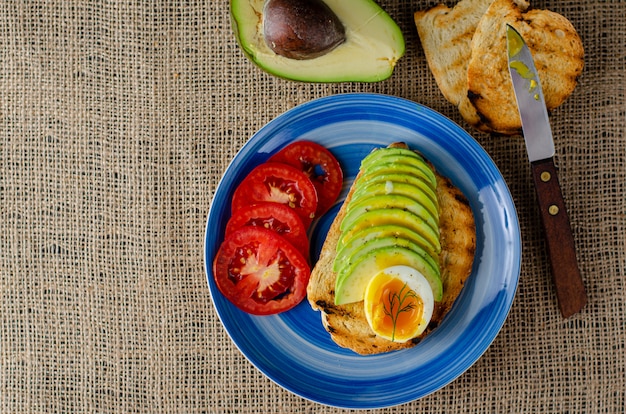 Panino con avocado a fette, uovo sodo e pomodori su tela di sacco. alimento dietetico equilibrato vista dall'alto. isolato su bianco