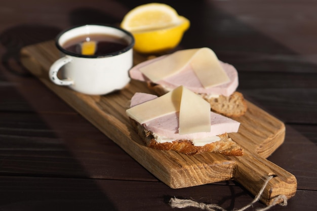 Panino con prosciutto a fette burro e formaggio su tagliere di legno vicino a una tazza di tè al limone