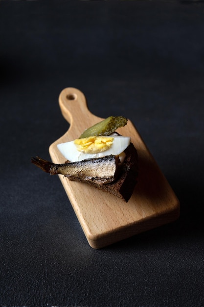 Sandwich with smoked sardine on a wooden board on a dark background flying food