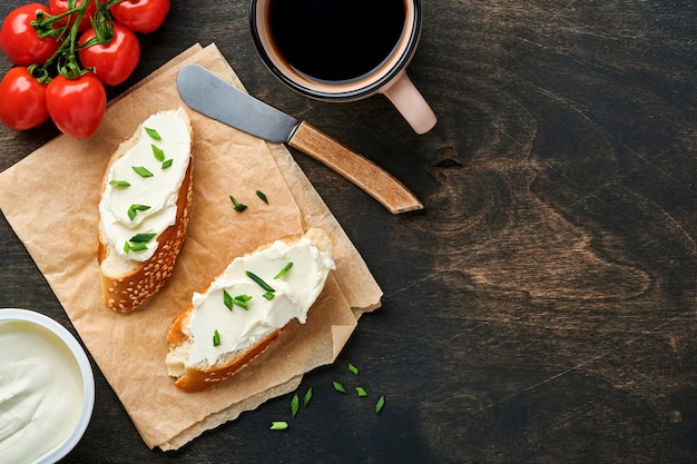 Sandwich with soft cheese with green onions and bread on dark wooden background. Simple breakfast with ricotta sandwich and coffee. Top view copy space for text.