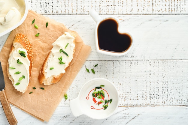 Panino con formaggio a pasta molle con cipolle verdi e pane su vecchio fondo di legno bianco. colazione semplice con panino alla ricotta e caffè. copia spazio vista dall'alto per il testo.