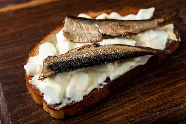 Sandwich with sprats, eggs and mayonnaise on wooden table.