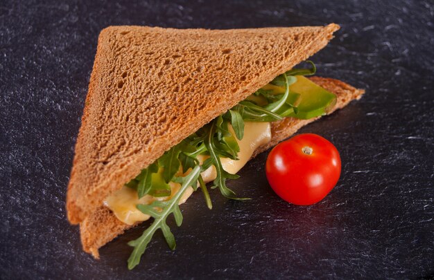 Sandwich with turkey breast, cheese, lettuce, arugula, tomatoes and onion on a black plate