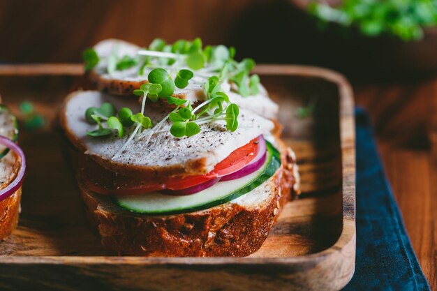 Sandwich with turkey breast and fresh vegetables served with microgreens on a wooden plate The concept of healthy and diet eating