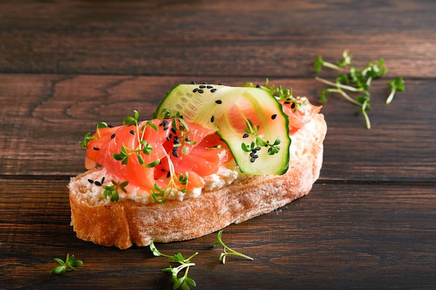 Sandwich zalm toast met roomkaas komkommer zwarte sesam en microgreens op oude houten tafel achtergrond Zeevruchten gezonde voeding fotografie in low key bovenaanzicht