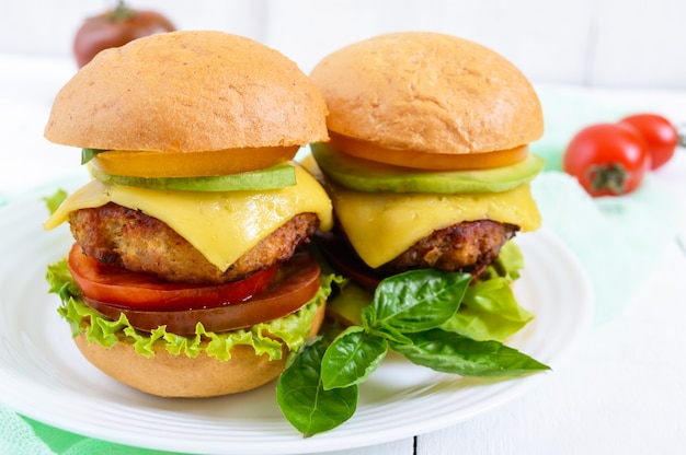Sandwiches (burgers) with yellow and black tomatoes, juicy cutlet, avocado on a plate on a white wooden.