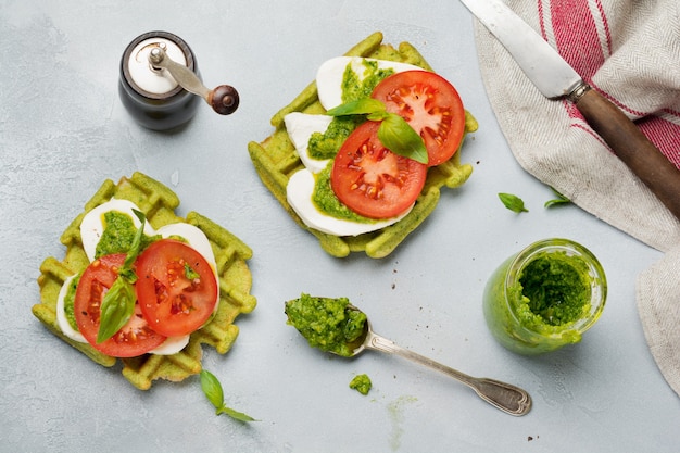 Sandwiches on green wafer with spinach and mozzarella cheese, pesto sauce, tomatoes and basil on a gray concrete old table. Selective focus. Top view.