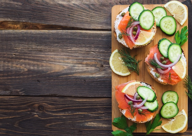 Sandwiches met gerookte zalm, rode ui, kappertjes, komkommer en citroen op rustieke houten.