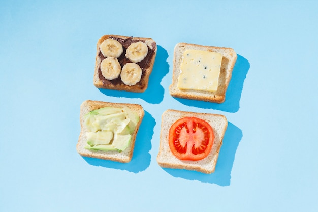 Sandwiches met kaas, tomaat, banaan en avocado op een blauwe ondergrond. Plat lag, bovenaanzicht.