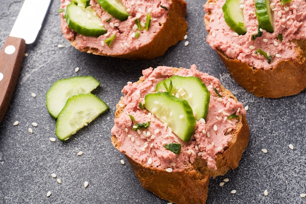 Sandwiches met kip pate en komkommer op donkere tafel.